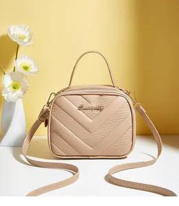 Close-up of beige crossbody bag featuring V-quilted faux leather and metallic logo detail