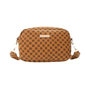 Brown camera crossbody bag with black clover patterns and a golden plaque on white background