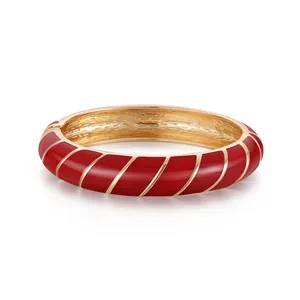 Elegante bracciale rigido dorato con strisce in smalto rosso su fondo bianco