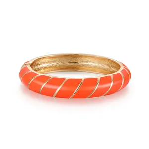Dettaglio di un bracciale rigido in smalto arancione con texture a spirale dorata