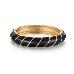 Dettaglio di un bracciale dorato con strisce in smalto nero e chiusura a scomparsa