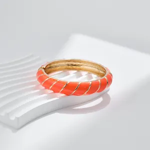 Dettaglio del bracciale in smalto arancione con strisce dorate su piedistallo ondulato