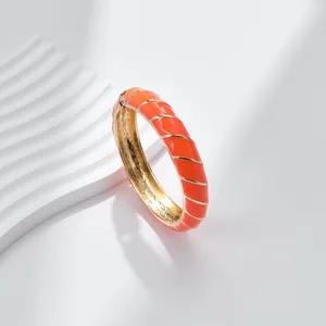 Dettaglio di bracciale rigido in smalto arancione e metallo dorato con motivo a spirale