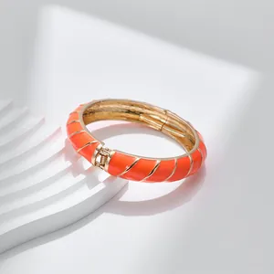 Dettaglio di un bracciale in smalto arancione con trama a spirale dorata e chiusura a molla