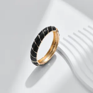 Dettaglio di un bracciale in metallo dorato con smalto nero su uno sfondo minimalista