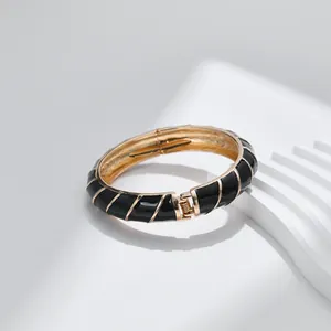 Elegante bracciale rigido dorato con smalto nero e linee diagonali con chiusura a molla