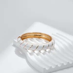 Dettaglio di un bracciale dorato con spirale in smalto bianco su un supporto espositivo