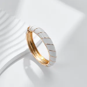 Dettaglio di un bracciale dorato con motivi a spirale in smalto bianco e cerniera laterale