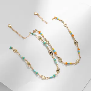 Detalle de tobillera bañada en oro de 18K con cuentas de colores y dijes de ojo