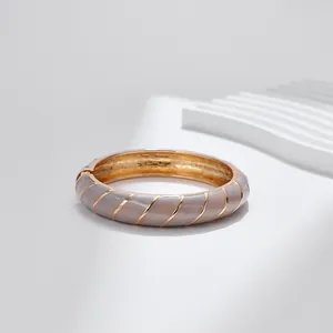 Dettaglio di un bracciale a cerniera dorato con smalto grigio e strisce geometriche eleganti