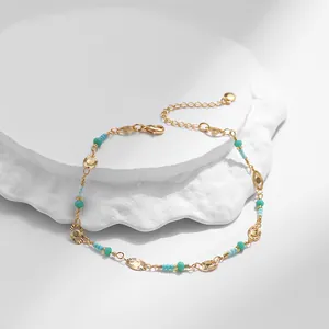 Detalle de tobillera bohemia de oro con cuentas turquesas y dijes de sol sobre piedra