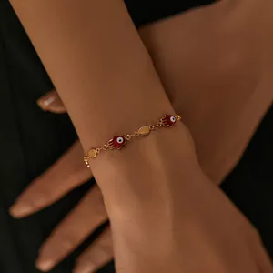 Detail of gold evil eye hamsa hand bracelet showing red charms on a female wrist