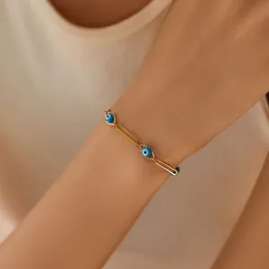 Detail of 18K gold-plated paperclip bracelet featuring three blue evil eye charms on a wrist