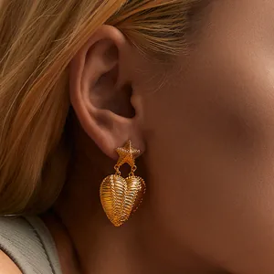 Close-up of gold 18k plated heart pendant earrings with textured stripes on model