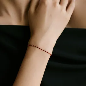 Detail eines 18 Karat vergoldeten Armbands mit zarten roten Perlenakzenten