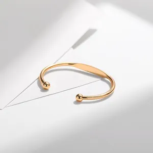 Minimalist gold-plated open bangle with polished spherical ends on geometric background