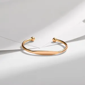Minimalist golden open cuff bracelet with small round beads on a clean geometric background