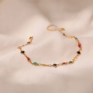 Golden chain anklet with colorful geometric glass stones on soft beige fabric