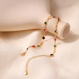 Gold plated anklet featuring multicolored glass stones draped on a white ceramic vase