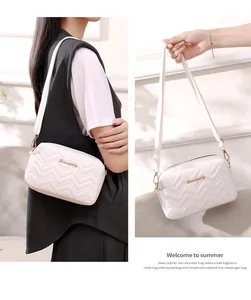 Detail of white wave-quilted crossbody bag with gold metal logo and slender shoulder strap