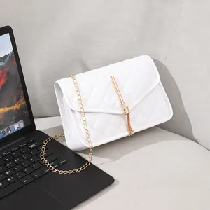 White quilted crossbody bag with gold chain strap and elegant tassel detail on sofa