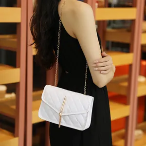 White quilted crossbody bag with gold chain strap and metal tassel on black dress