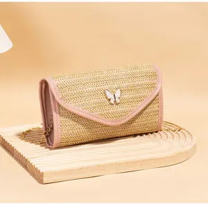Detail of woven straw envelope bag featuring a white butterfly clasp and pink leather trim