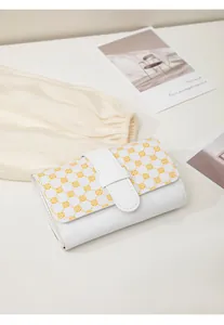 Detail of a white faux leather mini wallet featuring yellow clover pattern and buckle strap