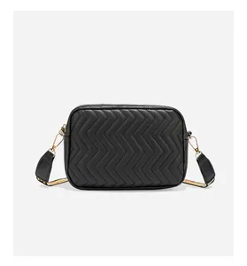 Detail van zwarte camera tas met chevron-stiksel, gouden hardware en brede schouderband