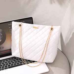 White quilted tote bag with gold chain straps resting on a laptop and sofa