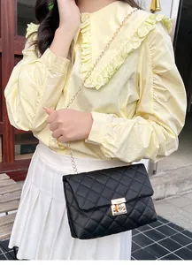 Close-up of black quilted shoulder bag with gold square lock and chain strap on model
