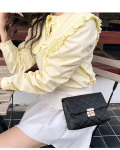 Detail of black quilted crossbody bag with gold chain strap and square metal lock closure