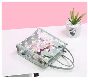 Detailed view of clear PVC daisy print handbag with cosmetics and green handle