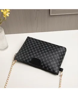 Detail of black crossbody bag featuring grey geometric patterns and gold chain strap