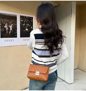 Brown quilted chain shoulder bag with square metal clasp worn over striped knit top