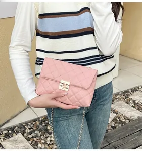 Detailed view of pink quilted chain bag with gold lock held by a model in casual outfit