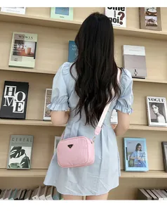 Pink woven texture camera bag with golden triangle logo and wide fabric strap detail
