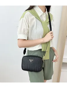 Detail view of black woven camera bag with gold triangle logo on a green dress model