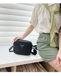 Detail of black woven crossbody camera bag with triangular metal logo on a beige shirt