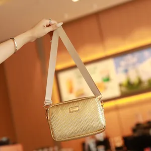 Bolso bandolera dorado trenzado con correa ancha y detalle de placa metálica frontal