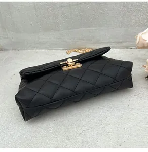 Detail of black quilted shoulder bag with gold twist lock and chain strap on grey stone