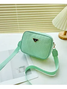Detail of light green woven texture crossbody bag with triangular metal logo and wide strap