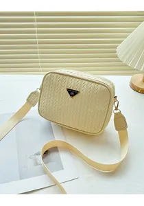 Detail of beige woven camera bag showing triangular metal logo and wide textile strap