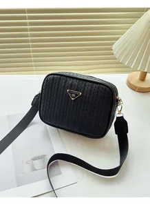 Close-up of black woven leather camera bag featuring gold triangle logo and wide strap