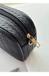 Close-up of black woven leather texture and elegant gold zipper on a compact camera bag