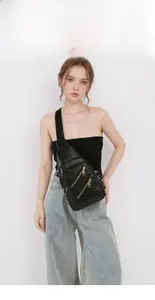 Detail view of black pebble leather crossbody chest bag with gold zipper compartments