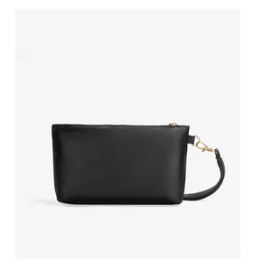 Detail of a minimalist black rectangle bag with a gold zipper and detachable wrist strap
