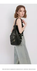 Detail of black lychee grain PU leather crossbody bag with golden metal zippers on model
