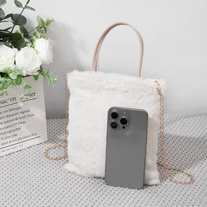 Mini borsa a tracolla in peluche bianco con catena dorata accanto a uno smartphone