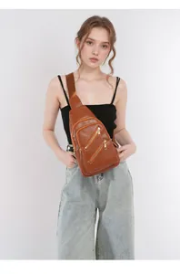 Detail of a brown leather chest bag showing metallic zippers and lychee grain texture